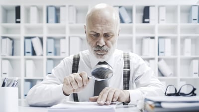 [Image] Older Man Examining Paperwork with Magnifying Glass | Audit Requirements for Nonprofit Charitable Solicitation Registration and Charitable Solicitation Renewal