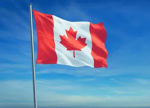 The Canadian flag with a red maple leaf on a white background, flanked by two vertical red bars, waves against a clear blue sky.