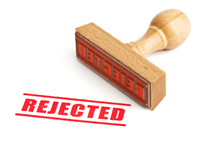 A wooden stamp, with the word "REJECTED" printed in red, is shown next to its impression on a white surface. The stamp face is angled upward, displaying the reversed text clearly.