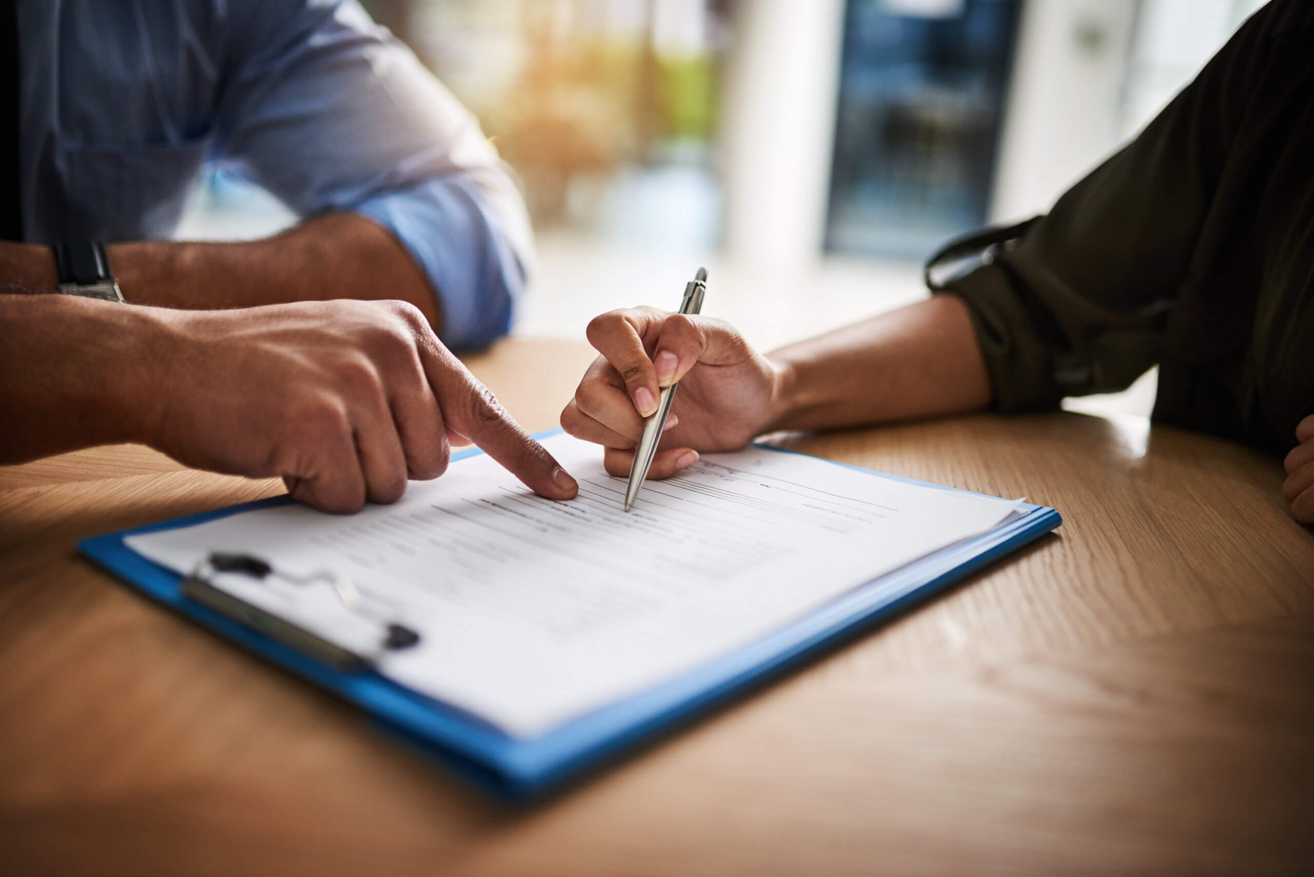 A person pointing at a pen on a clipboard.