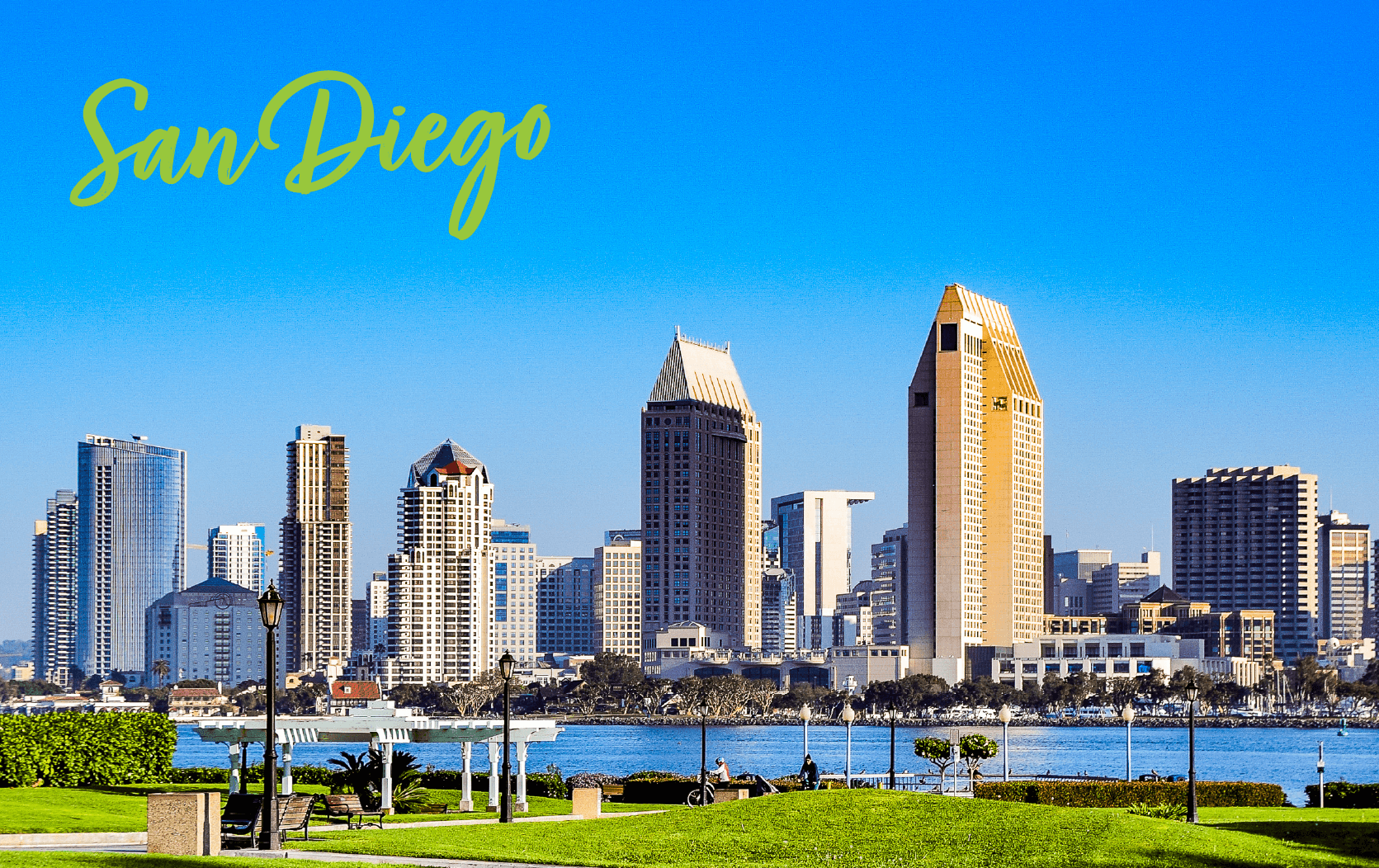 San Diego skyline with modern high-rise buildings under a clear blue sky, viewed from a park with green grass and benches across the water. "San Diego" in yellow script at the top left celebrates the Legal week Conference in this vibrant cityscape.