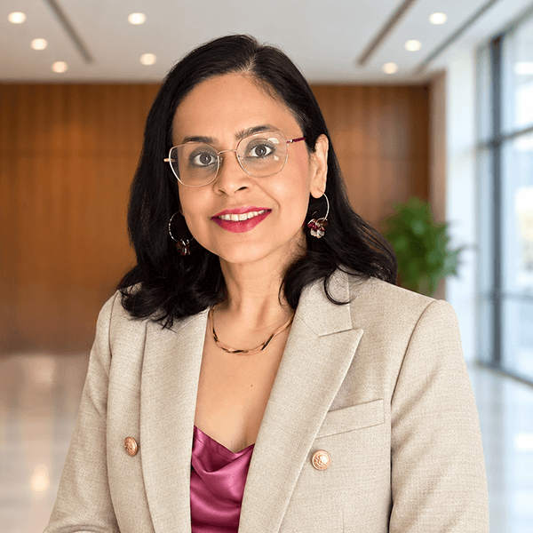 A woman with dark hair and glasses wears a beige blazer over a pink top while reviewing an effective financing statement for due diligence.
